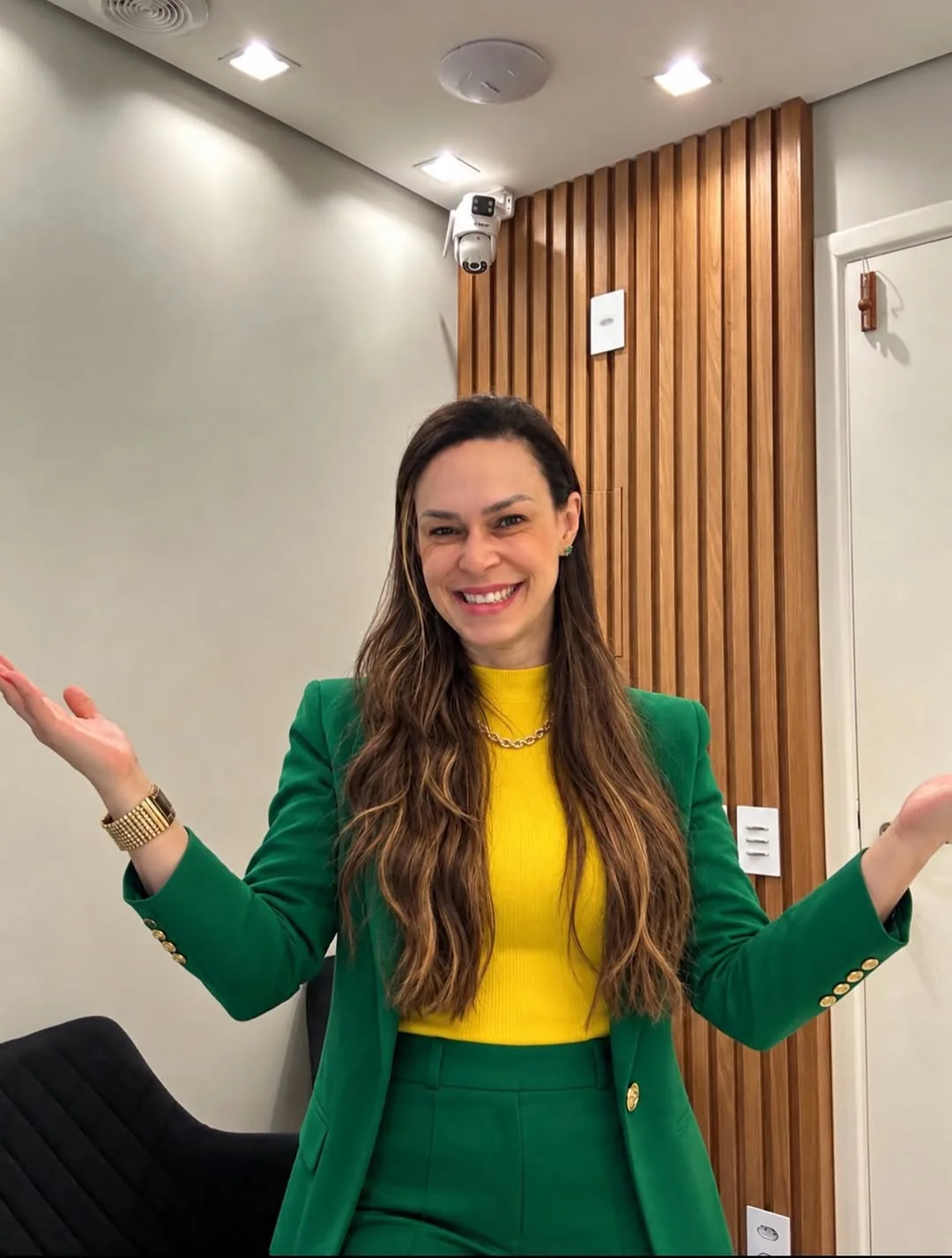 Dra. Mirian Bustillo sorrindo de braços abertos na clínica, de blazer verde